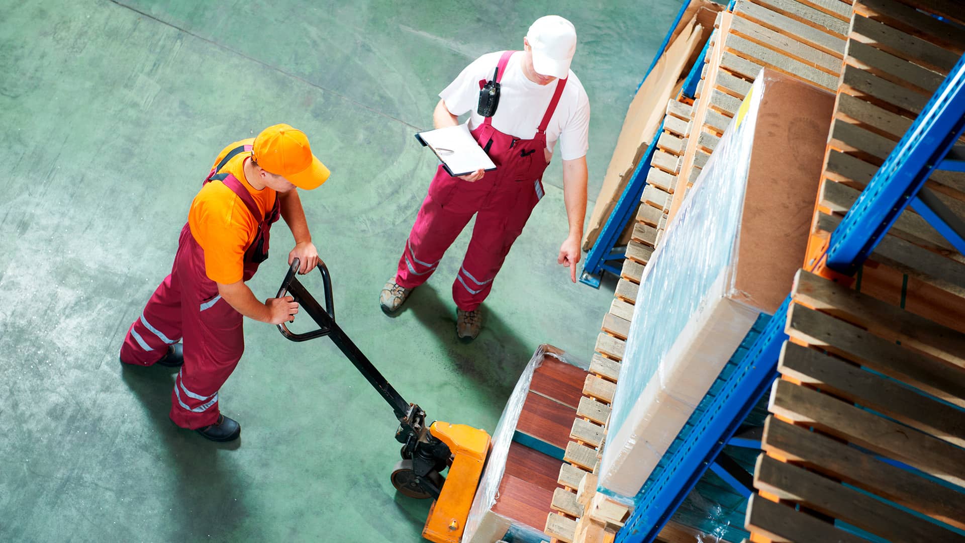 A warehouse worker using a manual lift while being evaluated by an inspector